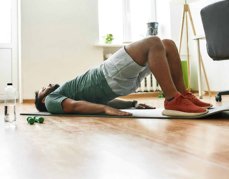 Man performing a glute bridge on a yoga mat—an exercise often used to activate pelvic floor muscles during Kegel routines for men’s sexual and vascular health.