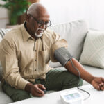 Man measuring his blood pressure at home while seated on a couch.