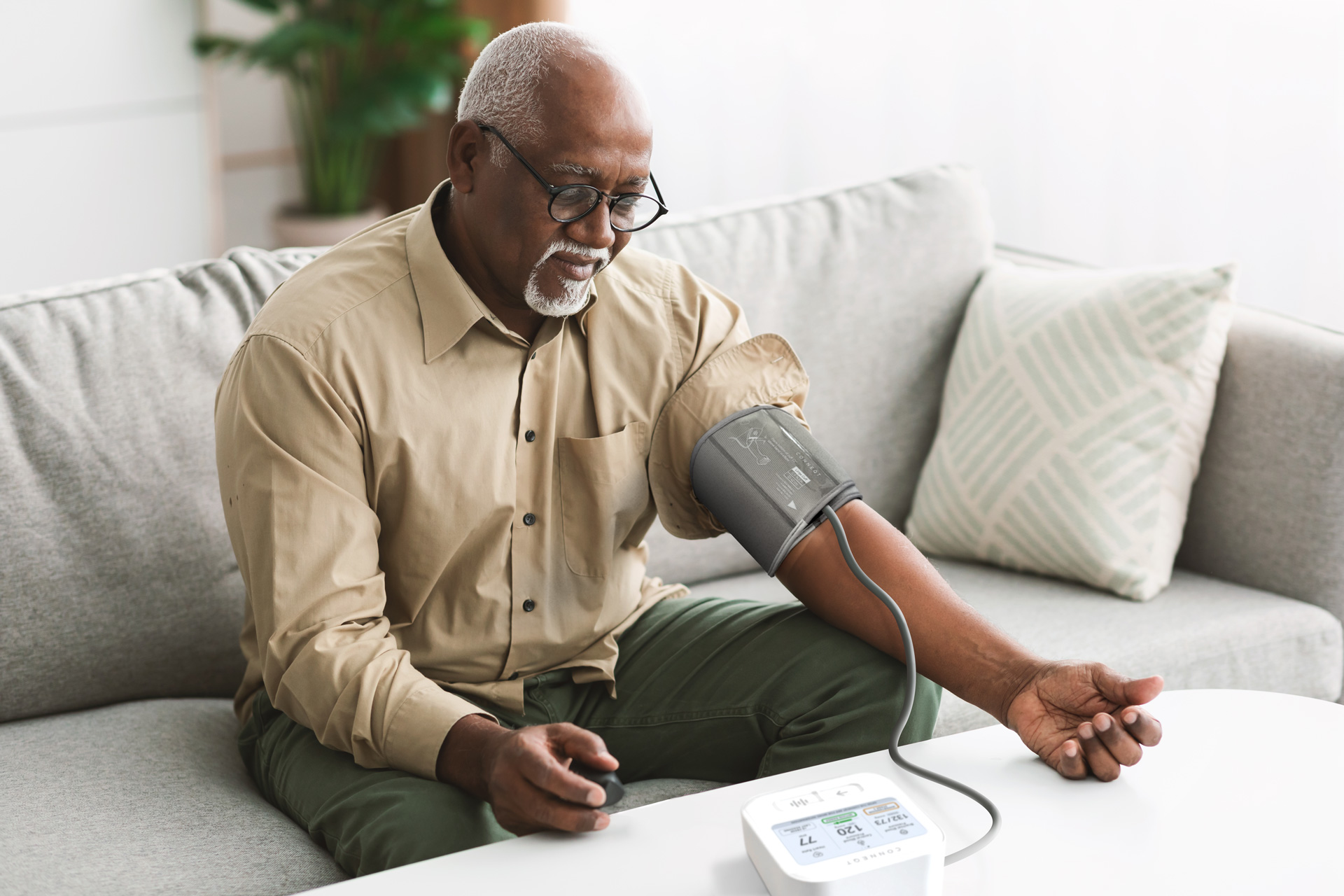 Man measuring his blood pressure at home while seated on a couch.