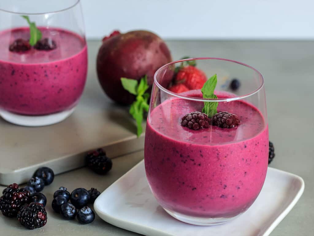 Two glasses of Blueberry and Beet Vascular Boost Smooth sitting on a table. 