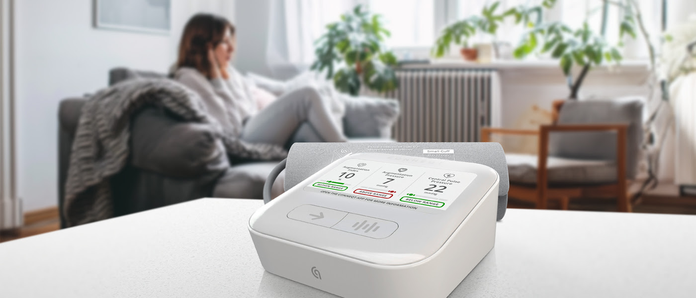 CONNEQT Pulse and its cuff on a table in a bright living room, with a woman relaxing in the background